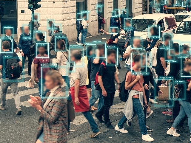Face detection and recognition of people who are walking through a street. There is a green rectangular outline around each person's head.  