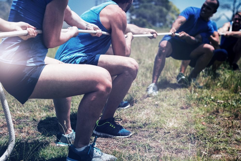 Group of people engaged in a tug-of-war, symbolizing the balance between AI in marketing and emotional intelligence. The image represents the competitive dynamic where technological advancements and human empathy must work together to achieve success in modern marketing strategies.