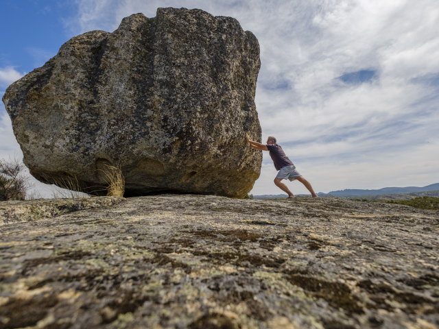 A man pushing a boulder without moving it - impossible task concept