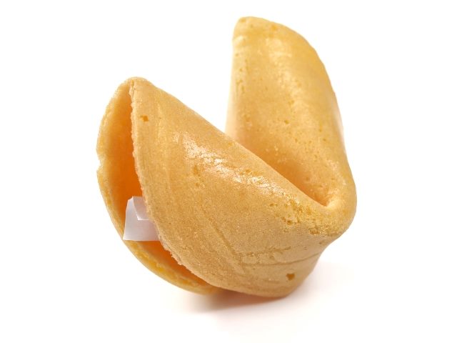 A closeup of a golden fortune cookie sitting its creased side down and pointed sides up and with a piece of the paper fortune inside visible on the left, on a white background.