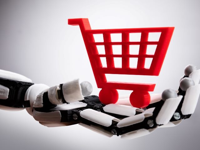 White and black robot hand holds red shopping cart. 