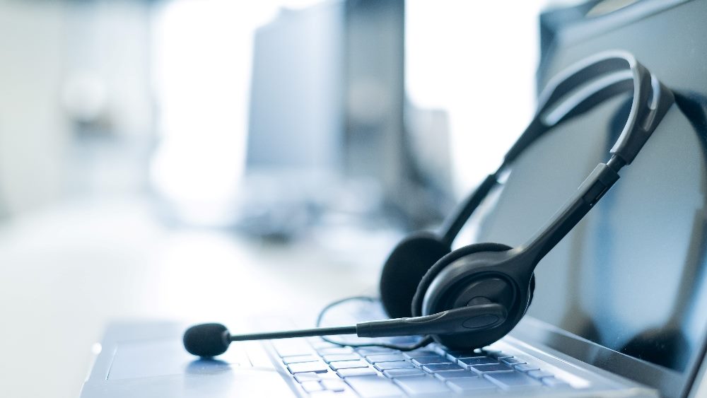 A laptop is open and a headset is sling across the screen top, suggesting improvements from AI in the contact center and AI in customer service.