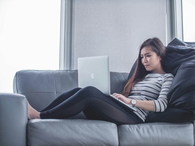A person uses a laptop computer on a couch.