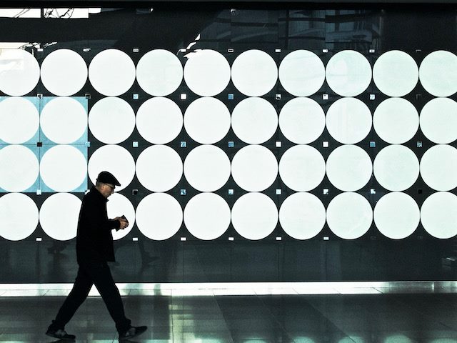 man walking up street looking down at phone with a wall covered in dots behind him