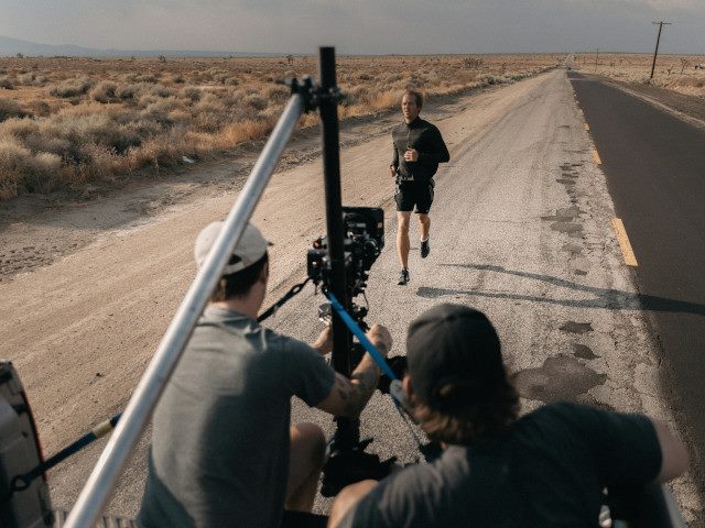 A film crew films an actor running on a road.