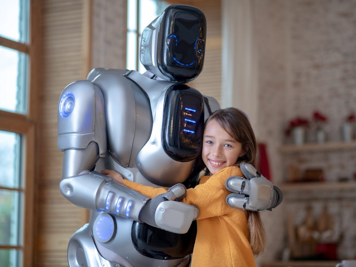 Child in a yellow sweater smiles while hugging a silver humanoid robot with glowing blue lights in a home interior.