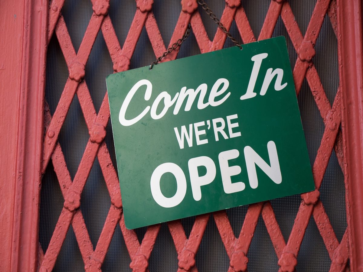 Text on a green plate "Come in we're open" hanging on the cafe entrance door 