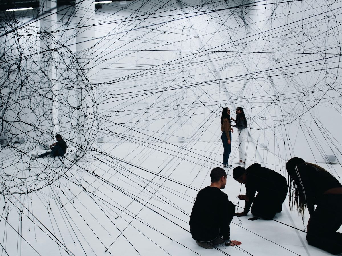 an abstract art show showing lines pulled across an open exhibit space, people fully immersed in the artwork