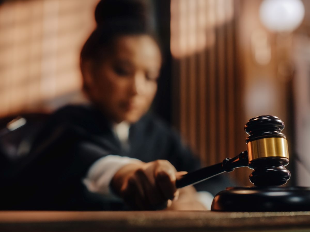 Judge striking a wooden gavel on a sound block in a courtroom, with the judge slightly out of focus in the background, symbolizing governance, authority, and oversight.