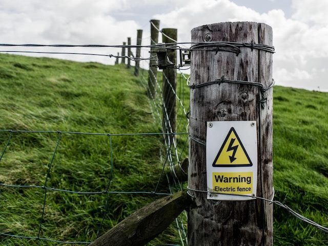 warning: electric fence sign on a post in the middle of a green field