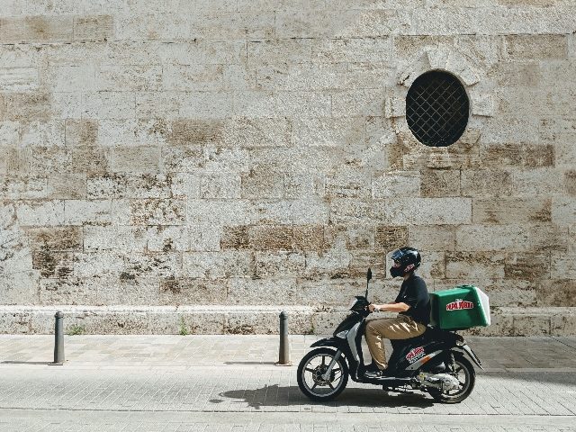 Delivery driver on a motorized bike with Papa John's delivery package on the back.