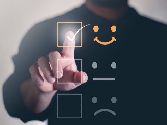 Person completing satisfaction survey with happy, neutral and unhappy options