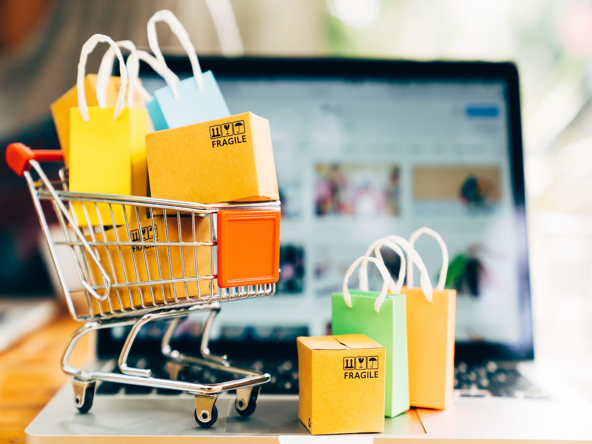 Mini product package boxes and shopping bags in a shopping cart sitting on top of a laptop keyboard