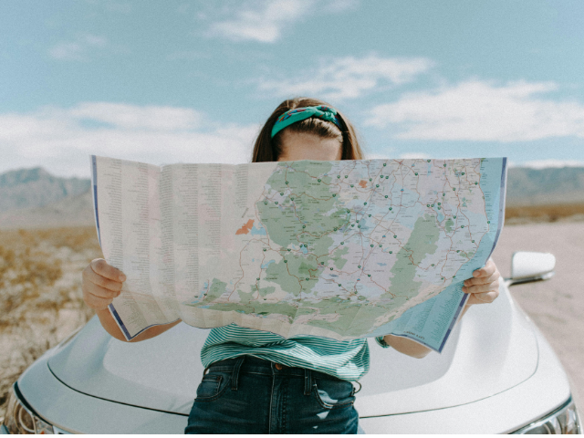 A person leaning against a car and reading a map 