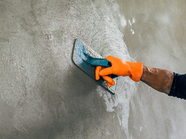  A worker's arm holding a plaster-smoothing tool on a residential building wall.