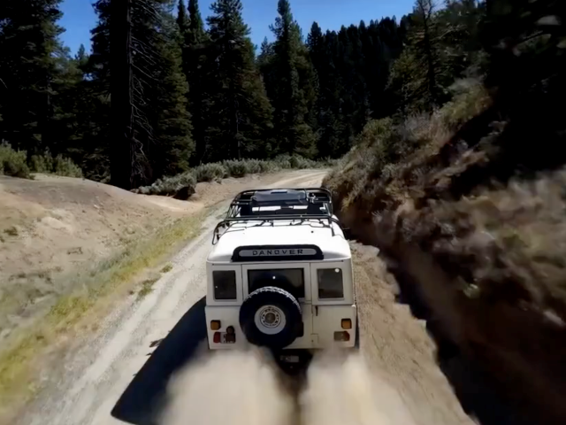 An old SUV drives on a dirt mountain road.