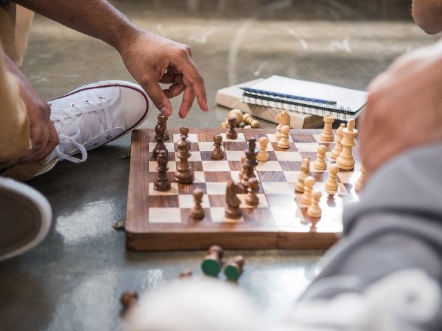 Men playing chess. We can only see their hands and one of their shoes. 