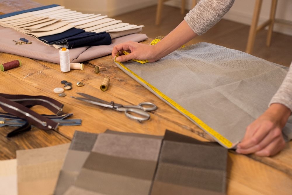 A person measuring fabric on a wooden table, surrounded by sewing materials like scissors, threads, and buttons. The scene illustrates precise tailoring, symbolizing the meticulous and customized approach of AI integration into journey orchestration in marketing strategies.