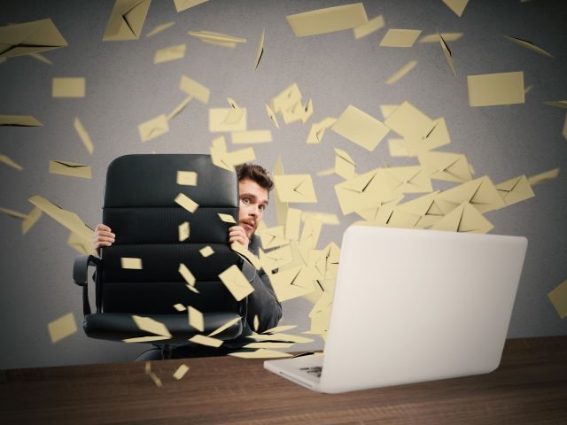 An office worker using his chair to protect himself from a barrage of spam emails shooting from his computer screen - email deliverability concept