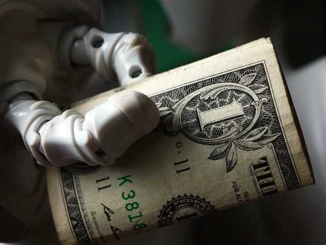 The image depicts a robotic hand with white casing, gripping a rolled-up one-dollar bill. The focus is tight on the robotic hand and the currency, with a softly blurred background, enhancing the stark contrast between the mechanical elements of the robot and the traditional paper money. This visual metaphorically suggests the economic activities or transactions involving technology,  in piece about the costs of the environmental impact of AI. 