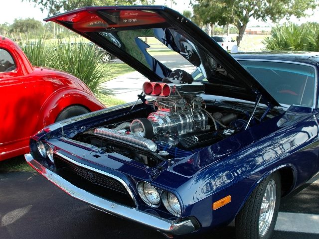 A dark blue vintage muscle car with the hood up at a car show displays a stock car motor suggesting looking under the hood at generative AI history. 