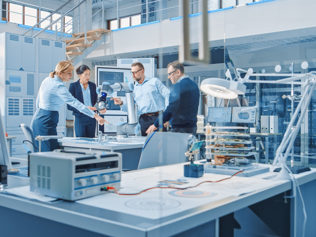 Workers gathered around a table working on a robotic arm. - Automated Workplace concept