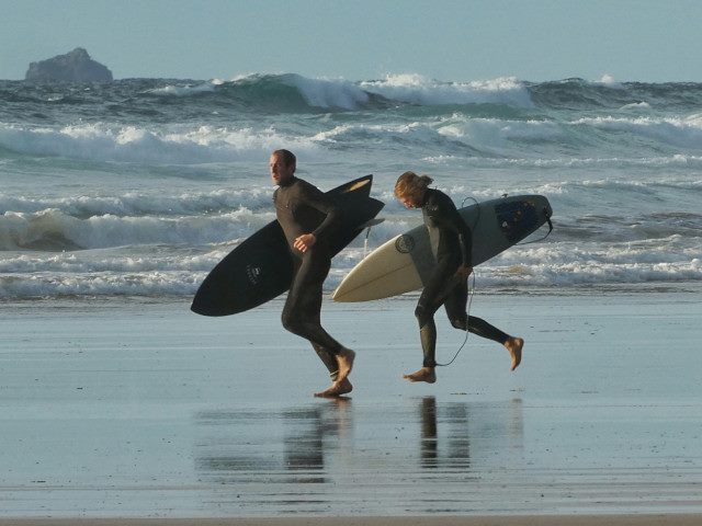 Two surfers run on a beach with their surfboards.