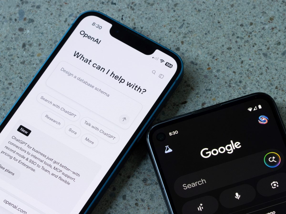 Smartphones side by side on a stone surface showing the OpenAI ChatGPT interface on one screen and the Google search interface on the other, illustrating competing approaches to AI-driven discovery and interaction.