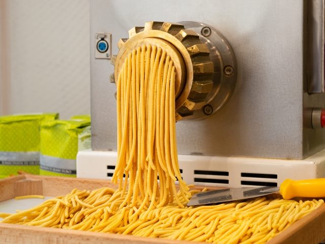 Pasta production with pasta being extruded and cut into smaller pieces.