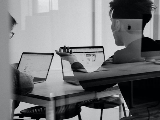man using a laptop and talking with a coworker at a table