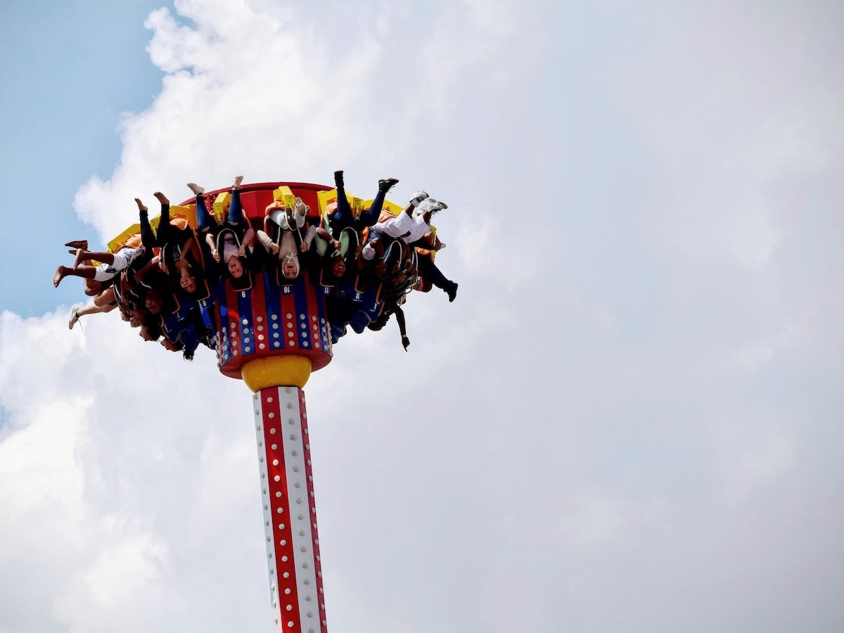 people on a ride, suspended upside down against a blue sky