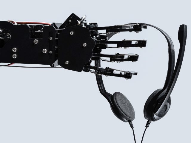 A black robot hand reaches out to hold a contact center headset, representing the increasing use of virtual agents in contact centers. 
