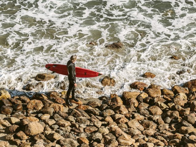 A surfer stands on the beach looking at the waves.