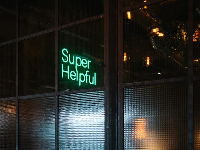 a peek into a commercial space with lit neon sign reading "Super Helpful"