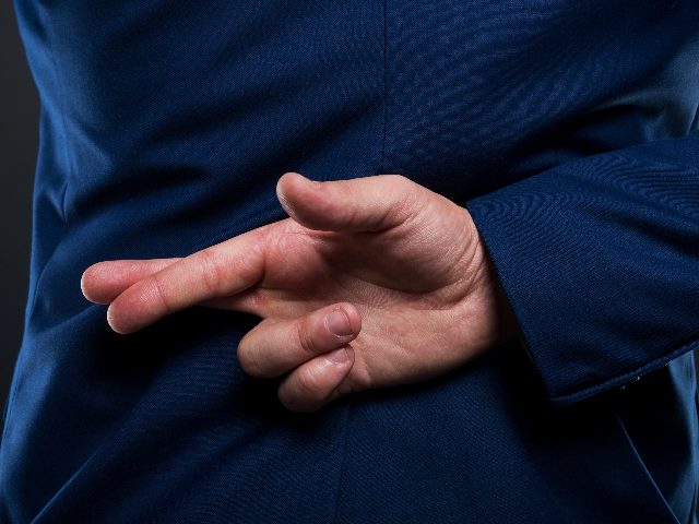 A person wearing a business suit holds his hands behind his back with crossed fingers in piece about AI development and ethical AI. 
