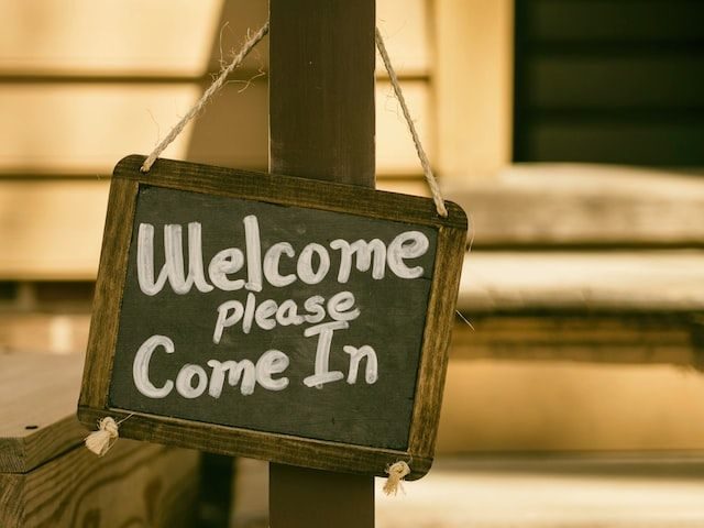 A sign hanging on a door that says "Welcome, please come in."