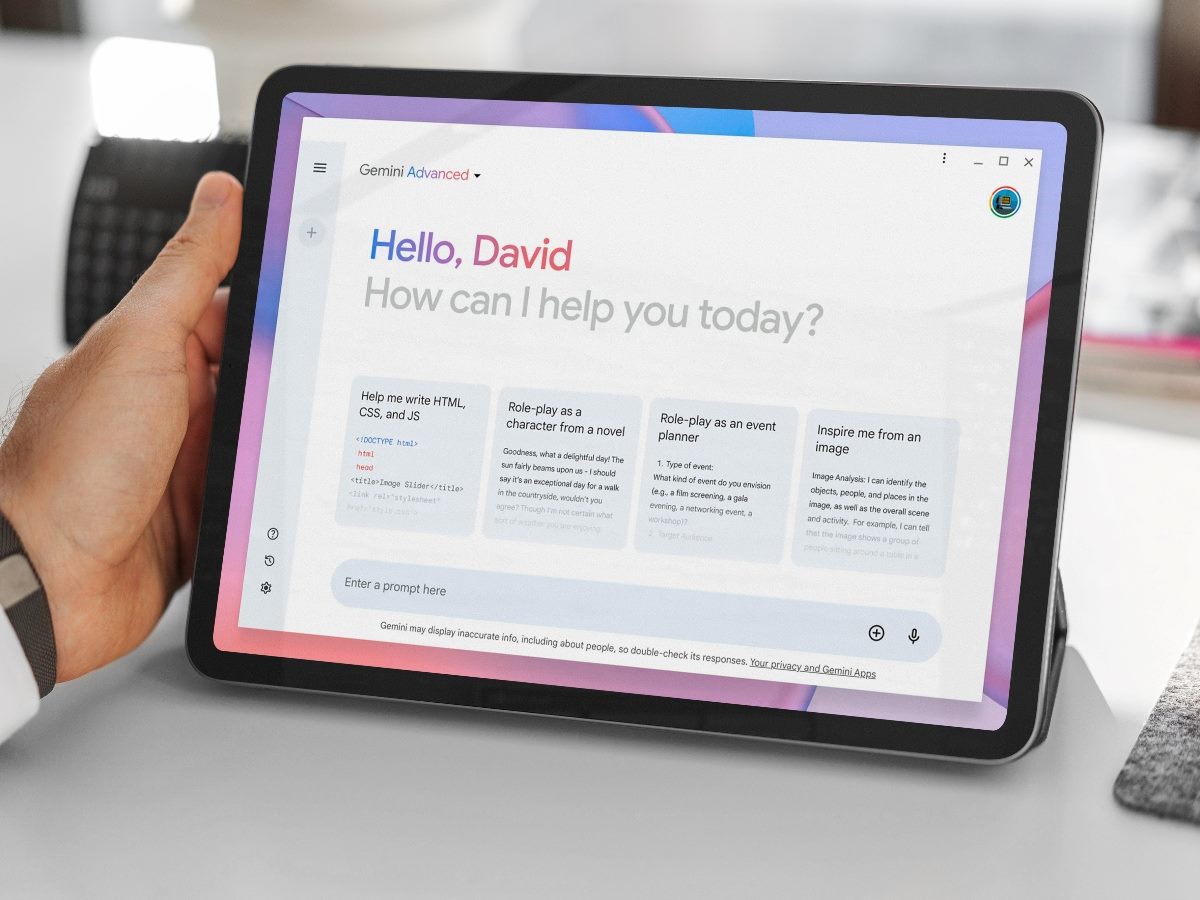 A person holds a tablet displaying the Gemini Advanced AI interface, with the screen greeting the user by name and offering prompt suggestions such as writing HTML, role-playing as a novel character, event planning, and image inspiration.