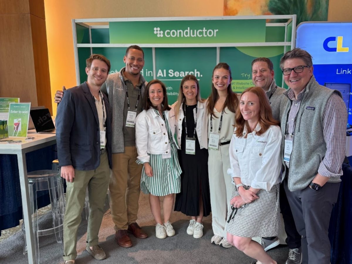 Group of Conductor team members standing together at the Conductor booth during SMX Advanced, with branded signage highlighting AI search and analytics in the background.