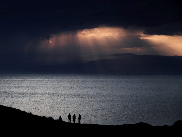 Four people backlit in an oceanfront sunset scene. Sunbeams break through the clouds at sunset. 