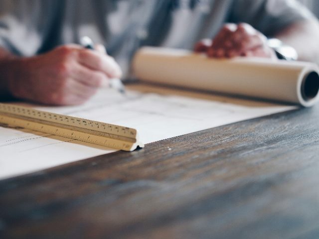 Someone's hand with a pencil in it analyzing blueprints.