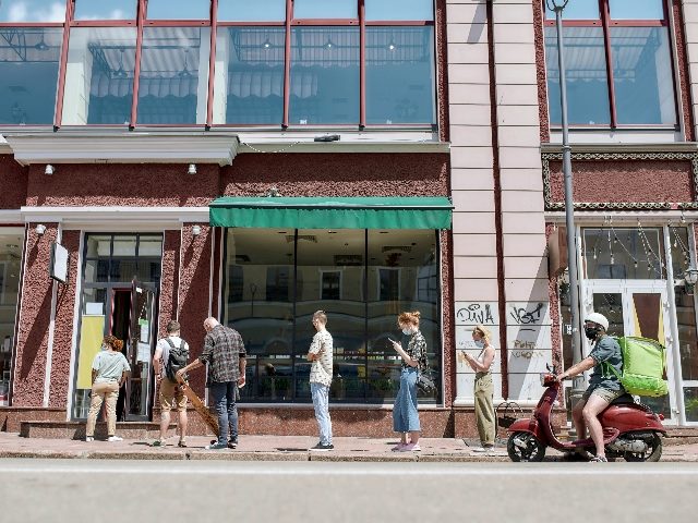 Full length shot of people wearing masks waiting in line, respecting social distancing to enter takeout restaurant or to collect purchases from the pickup point during coronavirus lockdown.