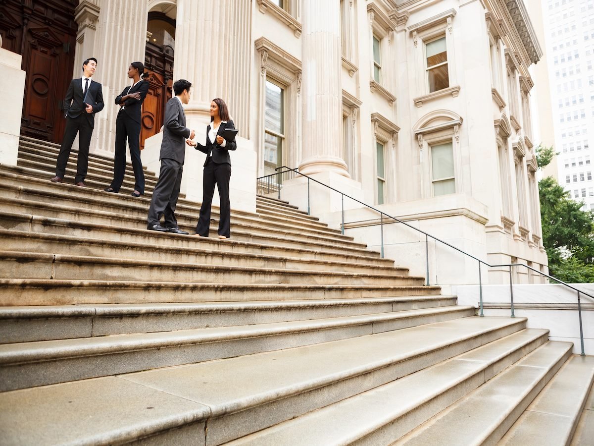 Four well dressed professionals in discussion on the exterior steps of a building