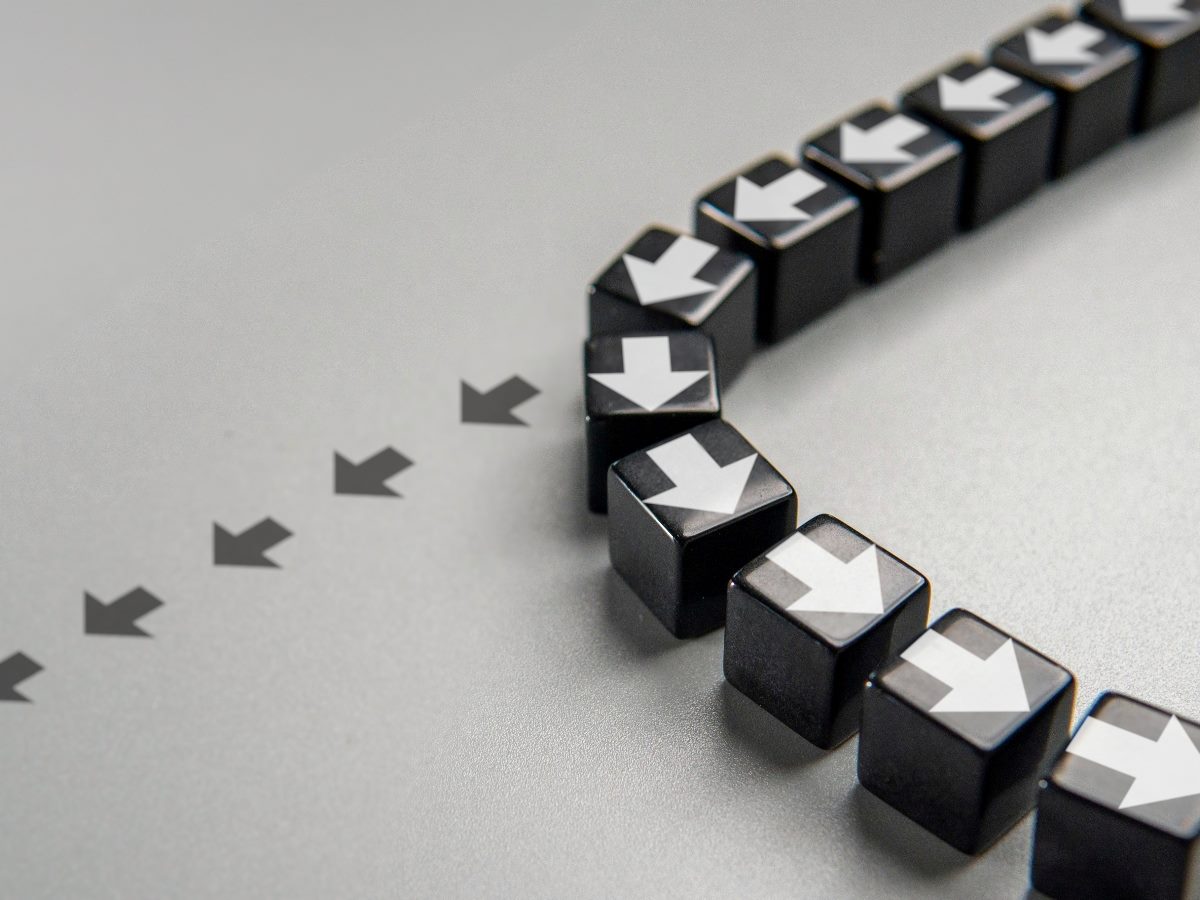 A curved line of black cube blocks with white arrows printed on top, showing a sharp change in direction from a straight path, symbolizing a strategic shift or change in course.