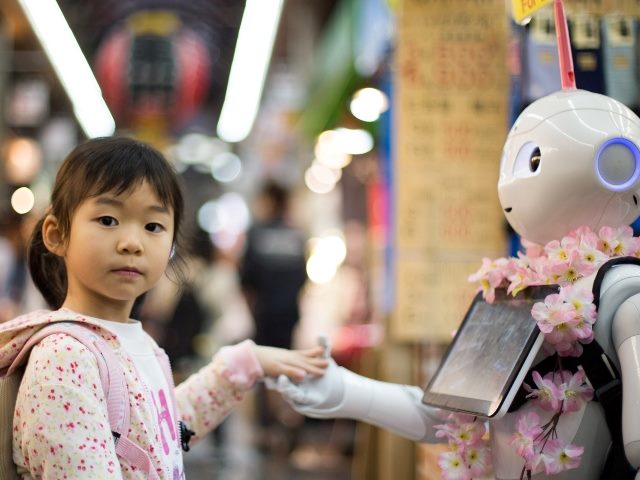 Young Japanese girl dressed in pink and white and carrying a backpack holds with robot wearing a lei  in Osaka market.