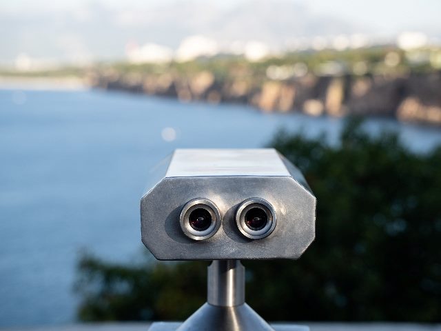 Coin-operated binoculars in front of mountains and sea.