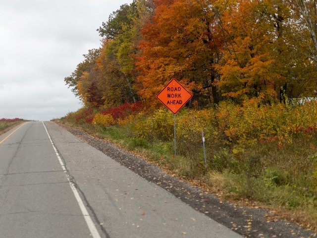  Scenic autumn road with a vibrant orange 'Road Work Ahead' sign amidst colorful fall foliage.