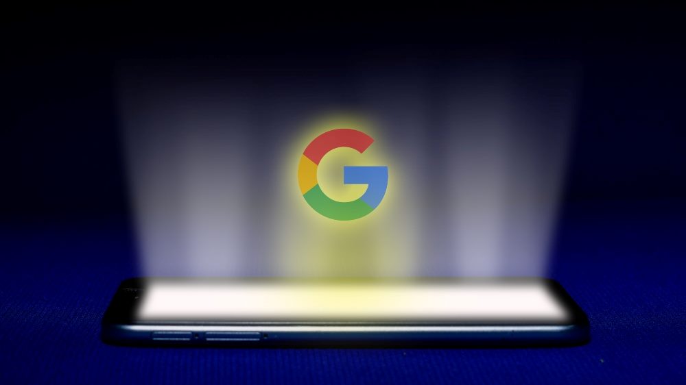 Hologram of Google logo in red, yellow, green and blue projected into the air on a dark blue backgrounds, representing Google privacy issues and risks.