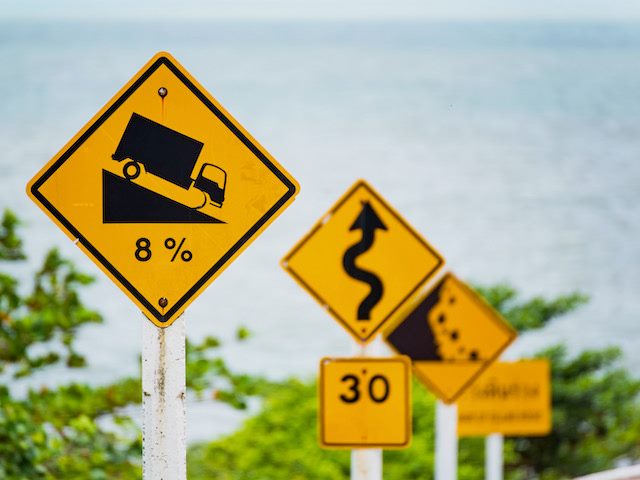 a series of road signs, warning of steep grades, twisty roads and falling rocks ahead