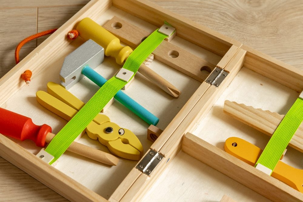A wooden toy toolbox that includes a flathead screwdriver, a Phillips screwdriver, a hammer and pliers in piece about generative AI tools.