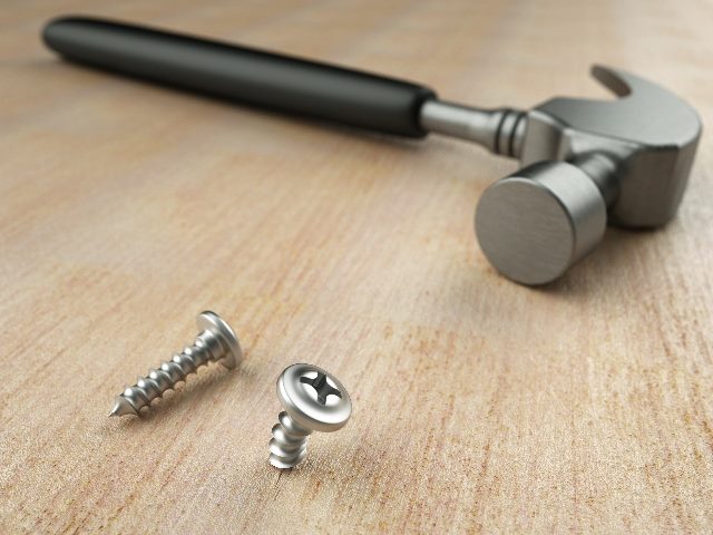 A hammer lies on a wooden surface with two bent screws in front of it, suggesting the misuse of AI in CX automation.